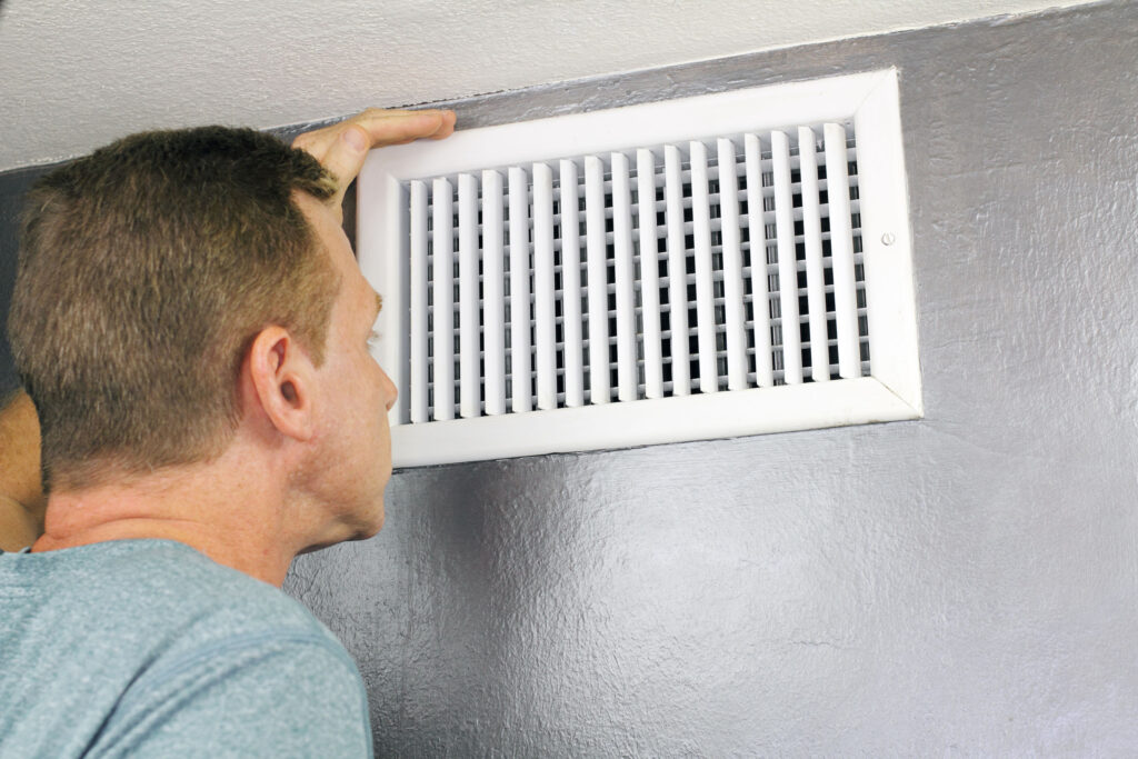 man examining an outflow air vent grid and duct
